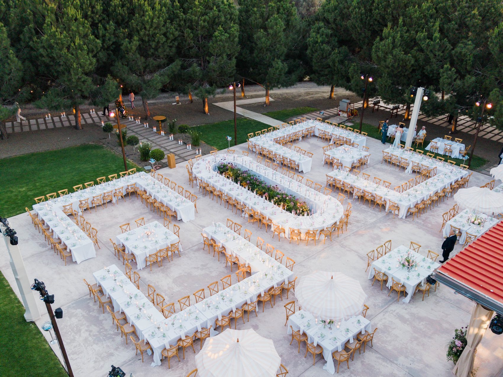 The Heritage venue from above, set for a banquet: long tables and white parasols among pine trees